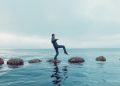 Man walks carefully on a path of small rocks in the middle of the sea; private equity must deal carefully with sanctions
