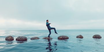 Man walks carefully on a path of small rocks in the middle of the sea; private equity must deal carefully with sanctions