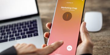 Concept image showing an office setting where a professional is receiving an unwanted robocall on her phone. The network provider detect the scam and put marketing crap notice. woman rejects the call.