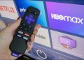 Roku remote in hand in front of a Roku home screen.