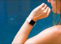 An Apple Watch on a woman's wrist, with blue water in the background.