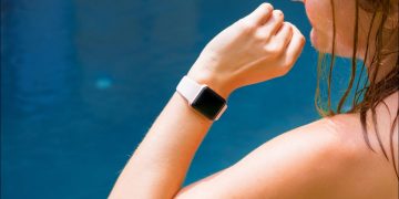 An Apple Watch on a woman's wrist, with blue water in the background.