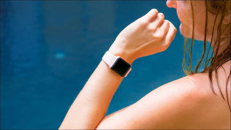 An Apple Watch on a woman's wrist, with blue water in the background.