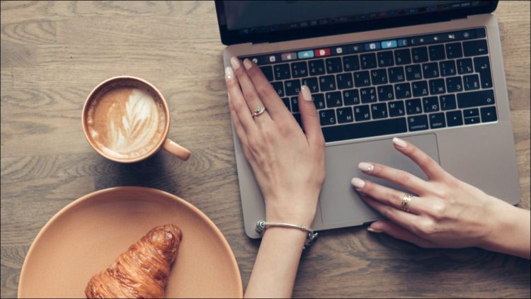 Hands on a MacBook keyboard alongside a coffee and croissant.