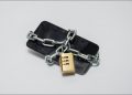 Smartphone wrapped in a metal chain with a padlock securing it.