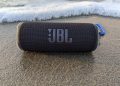 A JBL Flip 6 Bluetooth speaker sitting on wet sand by the ocean.