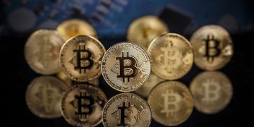 Many gold bitcoins staying on reflective surface with a single bitcoin in sharp focus