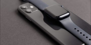 A black Apple Watch Series 7 on top of a matching iPhone 11.