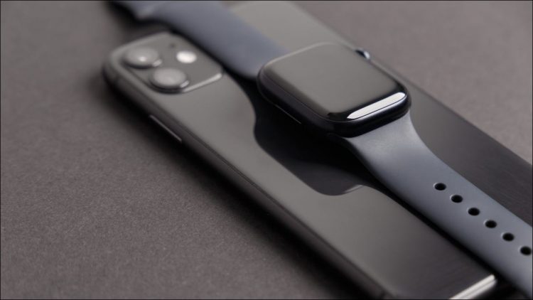 A black Apple Watch Series 7 on top of a matching iPhone 11.