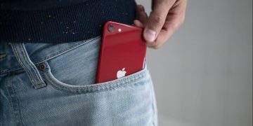 A red iPhone SE (2022 version) being pulled out of a person's jean pocket.