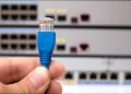A person's hand holding an Ethernet cable connector in front of internet switches.