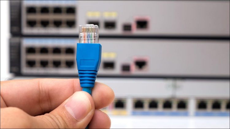 A person's hand holding an Ethernet cable connector in front of internet switches.