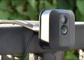 A flexible wire camera mount, holding a Blink security camera on a wide metal railing.