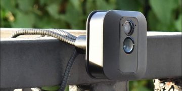 A flexible wire camera mount, holding a Blink security camera on a wide metal railing.
