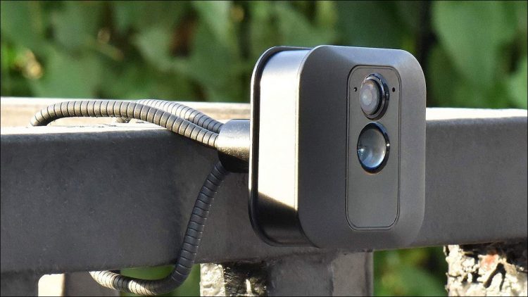 A flexible wire camera mount, holding a Blink security camera on a wide metal railing.