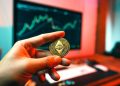 A man's hand holds an etherium coin at a computer table, Markets: Etherium Merge complete, ETH and linked tokens lift market