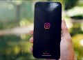 Person holding a phone with the Instagram logo visible. Header.