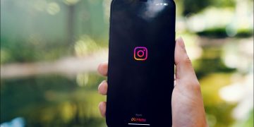 Person holding a phone with the Instagram logo visible. Header.