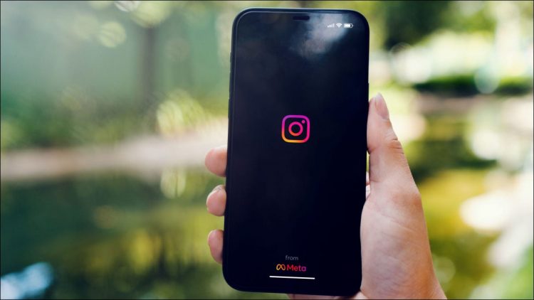 Person holding a phone with the Instagram logo visible. Header.