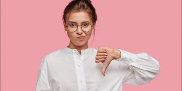 Young woman frowning in disapproval and giving a thumbs-down gesture.