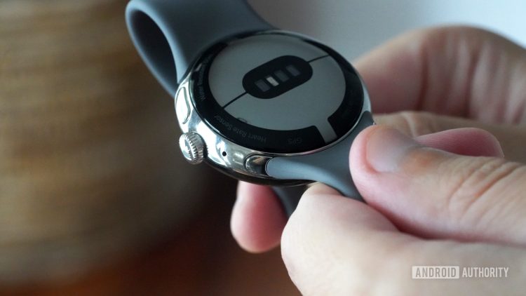 A user holds their Google Pixel Watch in hand illustrating how to find the band removal button.