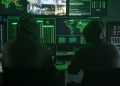 Team of Computer hackers coding on keyboard hidden in illegal hideout full of monitors