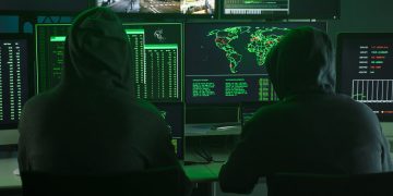 Team of Computer hackers coding on keyboard hidden in illegal hideout full of monitors