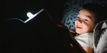 Child reading book in bed.