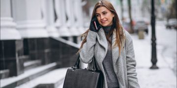 A woman wearing a winter coat and gloves, talking on her phone while walking down a snowy street.