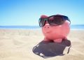 Piggy bank with sunglasses on the beach at the seaside