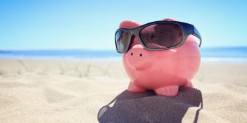 Piggy bank with sunglasses on the beach at the seaside