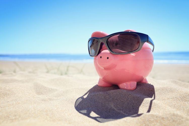 Piggy bank with sunglasses on the beach at the seaside