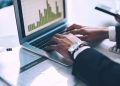 Hands type on the keyboard of a laptop displaying bar chart data / metrics / analytics.