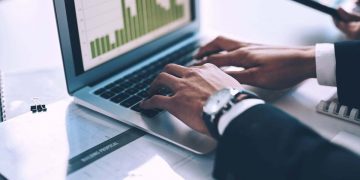 Hands type on the keyboard of a laptop displaying bar chart data / metrics / analytics.